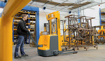 Worker pushing Jungheinrich walkie fork-over stacker toward metal rack